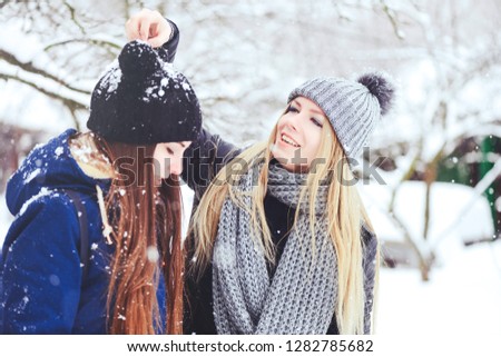 funny and happy two beautiful girlfriends play in the snow in winter, a lot of snow and winter clothes. blonde and brunette caring and emotions.