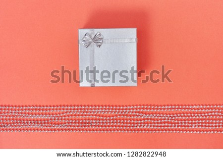 Bright silver closed gift box on paper background living coral colored. Minimal style composition.