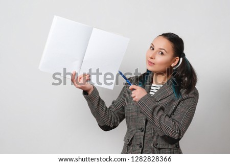 portrait of a young woman in a jacket on a light background. holding a notebook with blank place for copy space and shows pen.