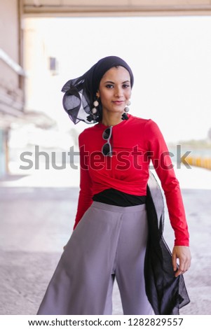 Fashion portrait of a beautiful Muslim Arab woman in an elegant outfit and a hijab headscarf walking down a car park during the day. She is tall and stylish. 