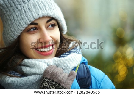 closeup horizontal image of a side looking happy smiling woman in warm winter clothes against the background of bright Christmas lights