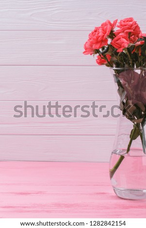 Red roses flowers in a vase. Cropped image. Pink wooden background.