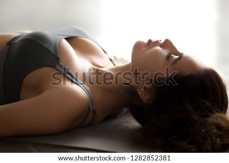 Young sporty attractive woman practicing yoga, doing Dead Body exercise, Savasana, Corpse pose, working out, wearing sportswear, grey top, indoor close up, at yoga studio Royalty-Free Stock Photo #1282852381