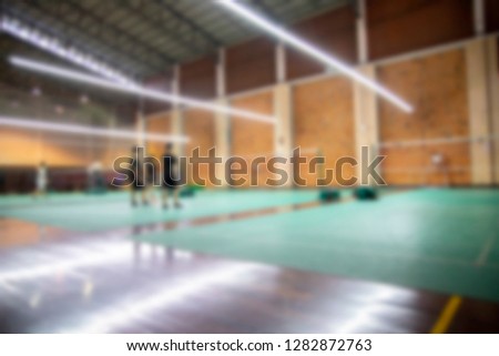 Blurred photo of badminton court. Field was cover with green rubber floor. Blurry photo use for background propose. Few players on the court prepare for competition. 