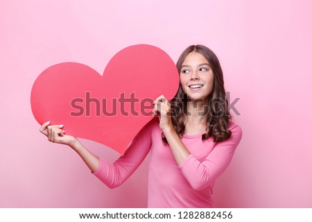 Young girl holding red paper heart on pink background