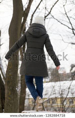 Back view of girl full of thoughts balanced on wooden bench in cold winter day above the city buildings. Sadly winter loneliness and depression. Warm clothes, life style. Search of inspiration.