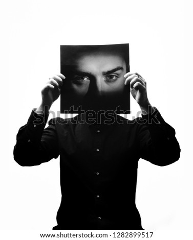 Black and white photo of man in the black shirt holding a photo with the face of a man in place of his face