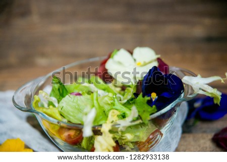 Spring vitamin salad: greens with cherry tomatoes and edible flowers (pansies) on a natural wood background. The concept of healthy eating.