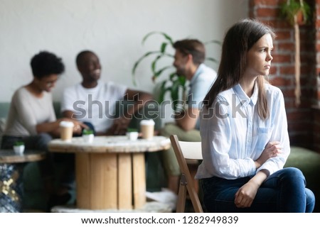 Multi-ethnic students spends free time in coffee shop, focus on sad teenage girl sitting on foreground apart from schoolmates feels lonely unhappy, thinking about negative relationships with coevals Royalty-Free Stock Photo #1282949839
