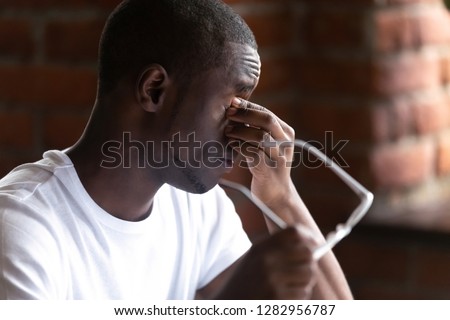 Close up black african man taking off glasses feels unhealthy suffering from eye strain after long working on computer. Poor vision and modern technologies negatively affecting to human health concept Royalty-Free Stock Photo #1282956787