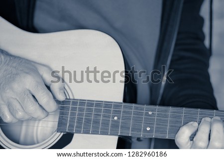 Young hands of the guitarist play the acoustic guitar, interpretation of the monochromatic shot. Royalty-Free Stock Photo #1282960186
