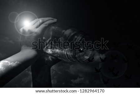 Close up of human hands holding a glass bottle and letting birds fly away with sky background and a sun flair on it.