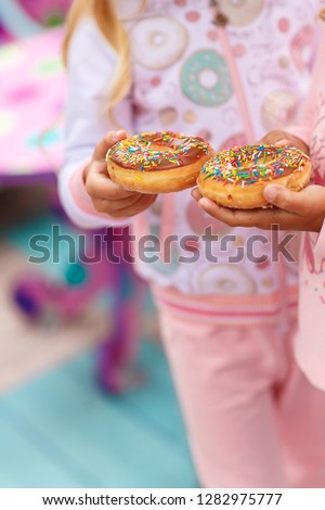 two girls are holding a sweet and a big donut decorated with pink icing and confectionary dressing