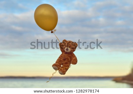  The little bear flies on a yellow balloon above the lake. Flight in a balloon.                       