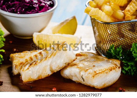 Fish dish - fried fish fillet french fries and vegetables on cutting board on wooden table