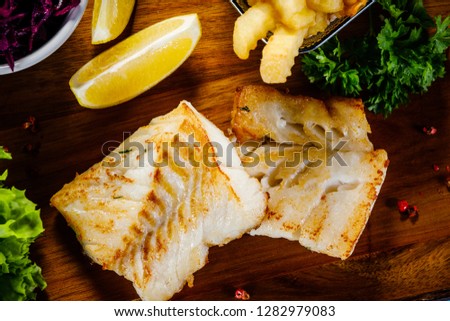 Fish dish - fried fish fillet french fries and vegetables on cutting board on wooden table