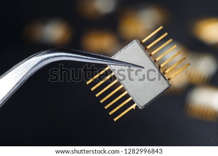 Golden electronic chip with tweezers on the dark background.