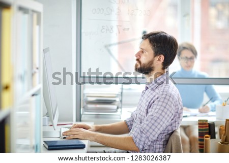 Serious manager or designer looking at computer screen while entering data or searching for websites in the net