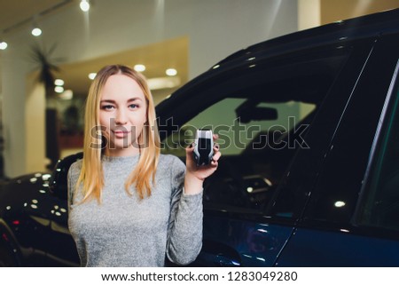 Happy woman holding keys to her new car at the dealership.
