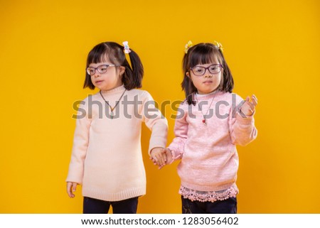 Soft warm sweater. Two young sister standing together and holding hands and wearing clear glasses for poor vision