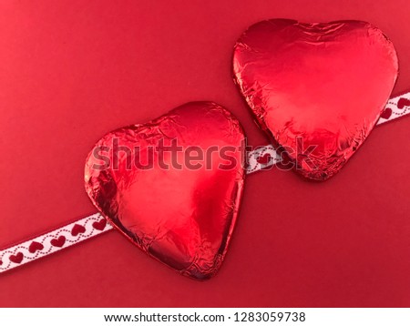 Chocolate hearts wrapped in red foil isolated on a red background with copy space