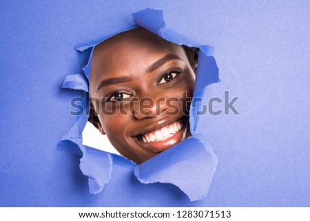 The face of a young african girl with a bright make-up and puffy purple lips peers into a hole in violet paper.