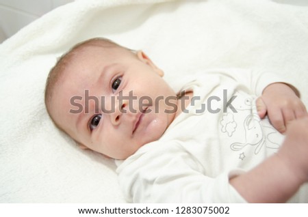 Cute tree months old baby boy dressed in white body looking at the camera while laying on the baby changer - bright white photo