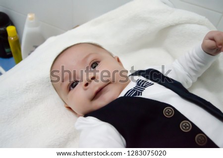 tree months old newborn baby boy dressed like businessman with bow tie, face expresion, laying on white baby changer