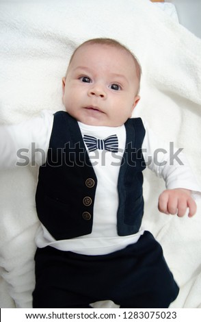 tree months old newborn baby boy dressed like businessman with bow tie, face expresion, laying on white baby changer