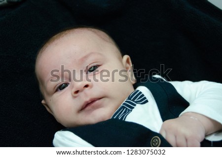 tree months old newborn baby boy dressed like businessman with bow tie, face expresion, laying on black baby changer