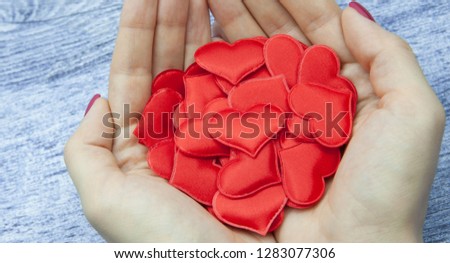 Close-up. Women's hands hold many red hearts in the palm against the wooden background of jeans color, the concept of saving love