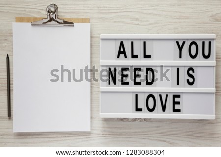 Modern board with text 'All you need is love', noticeboard with pencil over white wooden surface, top view. From above, flat lay, overhead. 