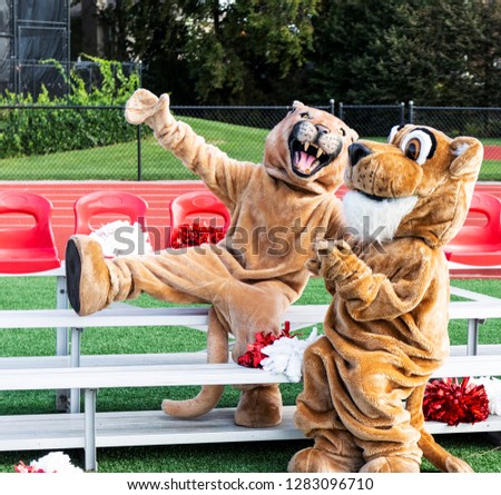 A male and female cougar mascots fool around for the camera while sitting on small portable bleachers Royalty-Free Stock Photo #1283096710