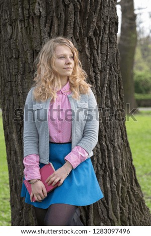 Girl with blonde hair based on the tree in park. Spring, sunny and daily light. Picture took in front of model.