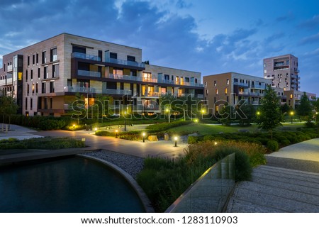 Green park with modern houses in the background in the evening. Illuminated green area with grass and trees. Royalty-Free Stock Photo #1283110903