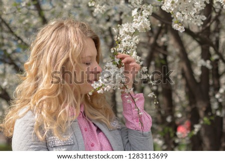 Girl with blonde hair smelling spring flowers. Spring, sunny and daylight. Picture was took from one side of the model.