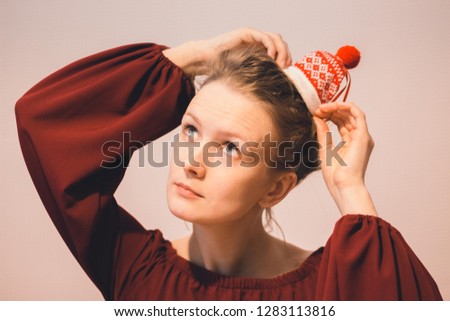 A beautiful young girl with big eyes is wearing a red sweater. On the girl's head are tied hairs in a bun on which a hat with Christmas patterns is worn.