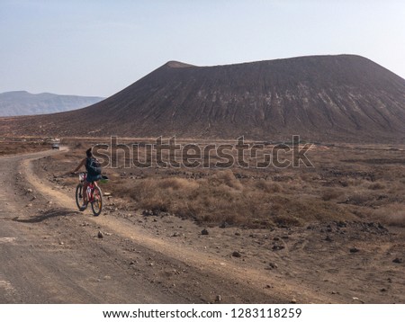 People cycling on a dirt path in the island of La Graciosa, Lanzarote, Canary Islands. Spain. In the background El risco, the mountainous part to the north of Lanzarote