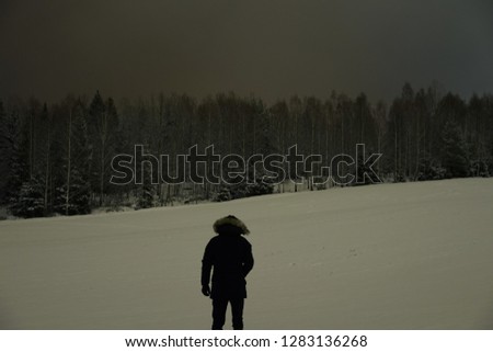 Man standing on the winter field in front of forest. Beautiful dark snowy winter night. Calm, peaceful abstract picture.
