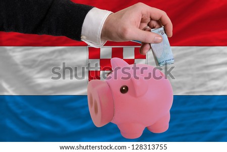 Man putting euro into piggy rich bank and national flag of croatia in foreign currency because of insecurity and inflation