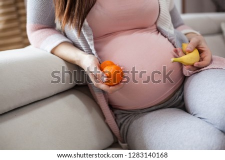 Close up of pregnant woman holding fruit.