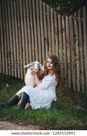 A girl in a white dress walks with a goat in nature. toning