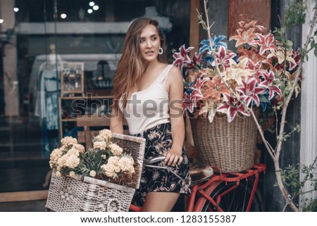 Beautiful brunette woman with colored makeup  on a red bike smelling flower, over marigold flowers field