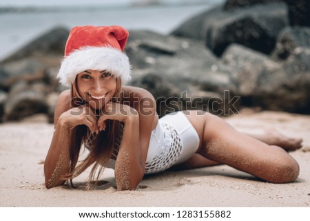 Young woman in white swimsuit and santa hat lying on the beach. Christmas vacation. Christmas beach vacation woman wearing Santa hat and bikini enjoying christmas on tropical beach. Phuket. Thailand