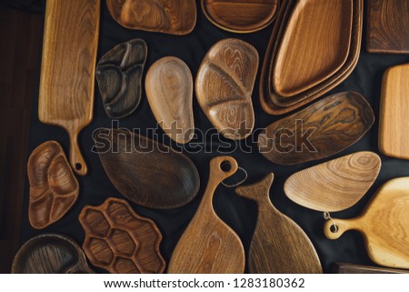 Top view of unused brand new brown handmade wooden kitchen utensil, made from different wood species, dish plate and cutting board on black background