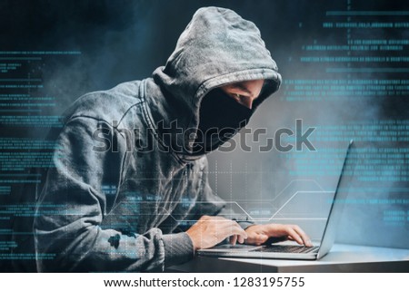 Male hooded hacker with hidden face accessing to personal information on laptop in the dark. Technologal, cyber crime concept. Digital background with binary code.

