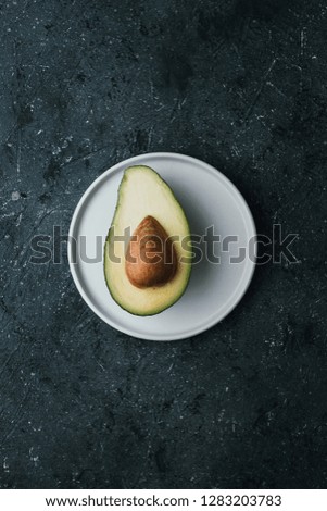 Ripe half avocado on white plate on dark background, top view