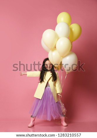 Little Korean baby girl in yellow fashion jacket and purple dress with balloons thumb up celebrate happy smiling on pink background