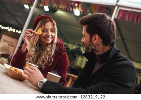 Young couple are drinking mulled wine with snacks at the street food market.