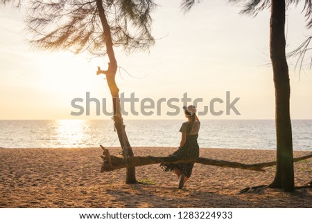 Happy young woman enjoying freedom  sitting on log viewing sunset on the sea sky sunset background